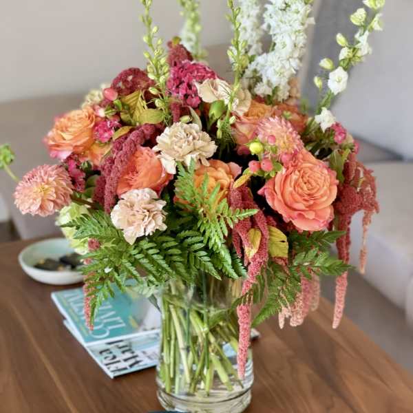 Mixed bouquet of peach and pink flowers in a clear glass vase