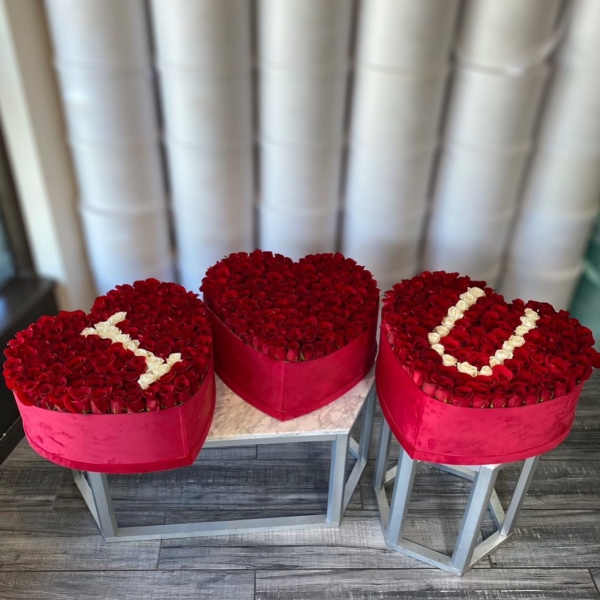 Three heart-shaped rose arrangements in red boxes on stands