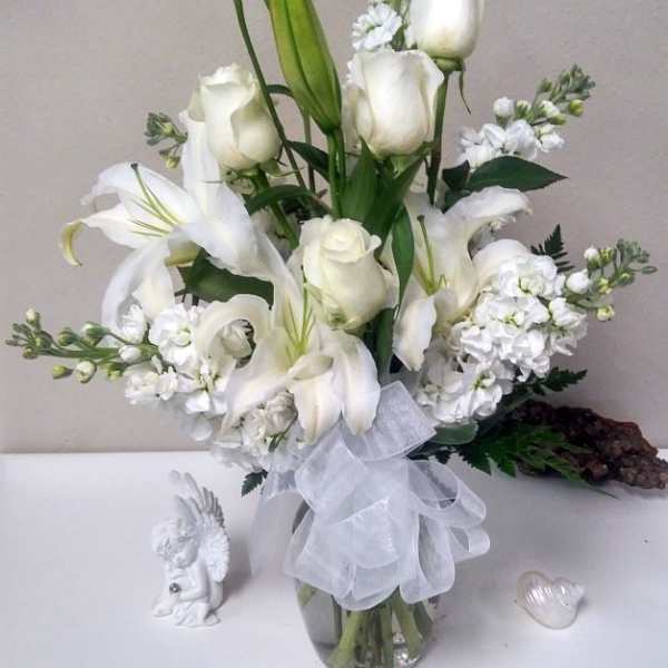 White lilies and roses arranged in a glass vase with a sheer ribbon