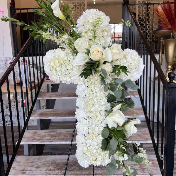White floral cross arrangement on an easel with roses and calla lilies