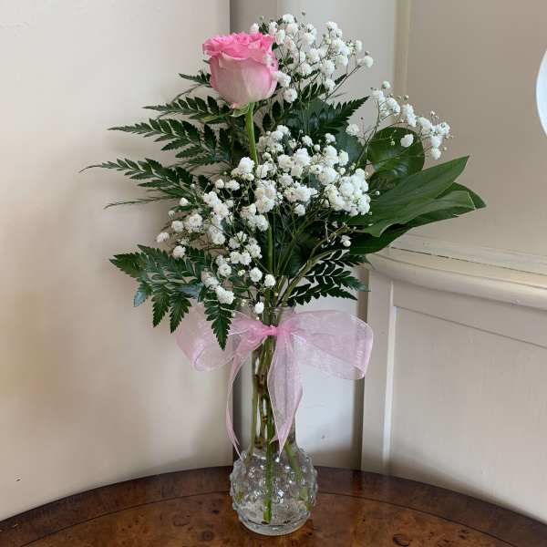 Pink rose in a clear vase with white baby's breath and a pink ribbon