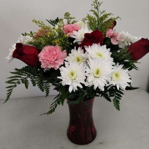 Arrangement of red roses, pink carnations, and white chrysanthemums in a red glass vase