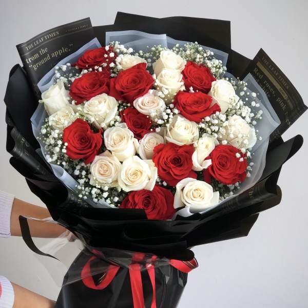 Bouquet of red and white roses wrapped in black paper with a red ribbon