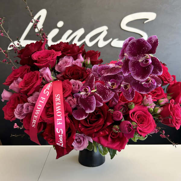 Bouquet of red roses and purple orchids in a black vase