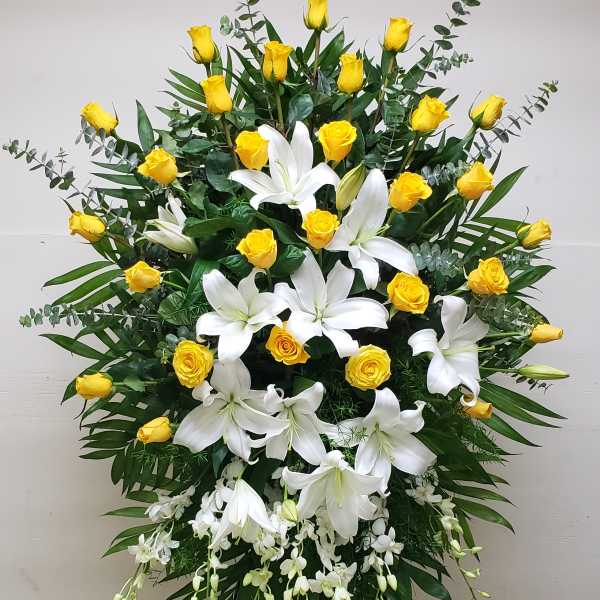 Standing spray of yellow roses and white lilies with cascading orchids on an easel
