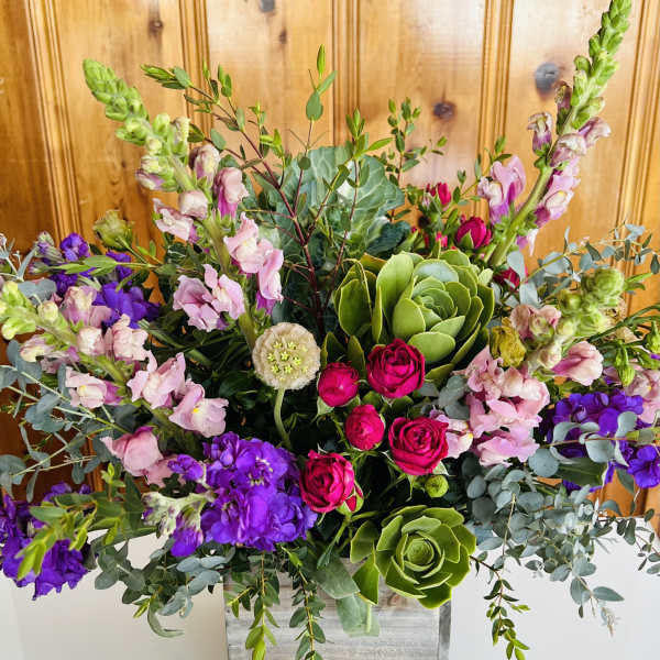 Mixed bouquet with pink roses, purple blooms, and green succulents in a wooden box
