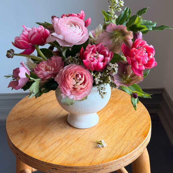 Pink floral arrangement in a white pedestal vase