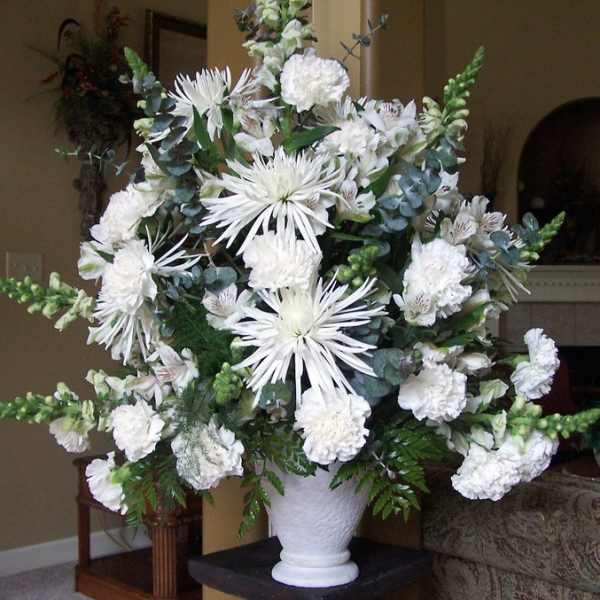 White floral arrangement in a white vase with spiky blooms and carnations