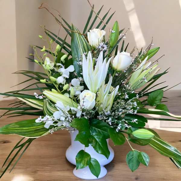 White lilies and roses in a white vase with long green leaves