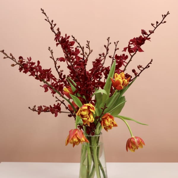 Tulips and burgundy orchid stems in a clear glass vase