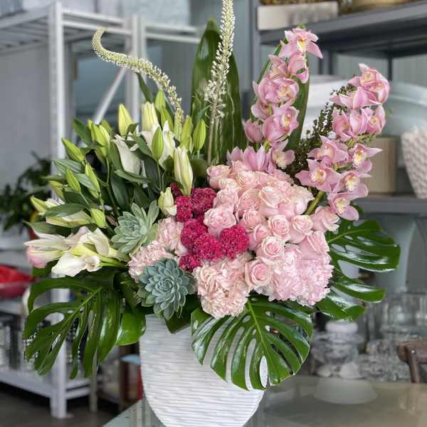 Pink and white floral arrangement in a white vase with large green leaves