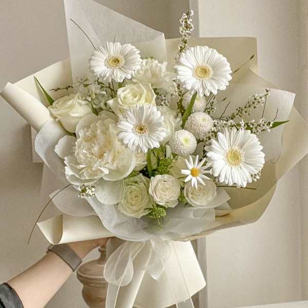 White bouquet with gerbera daisies and roses wrapped in cream paper