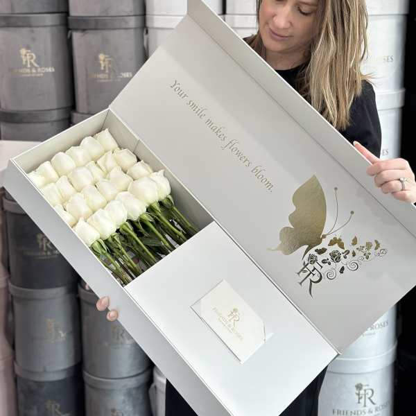 White roses arranged in a presentation box held by a woman