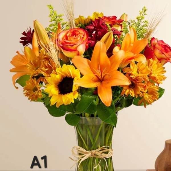 Bouquet of orange lilies, sunflowers, and red roses in a glass vase