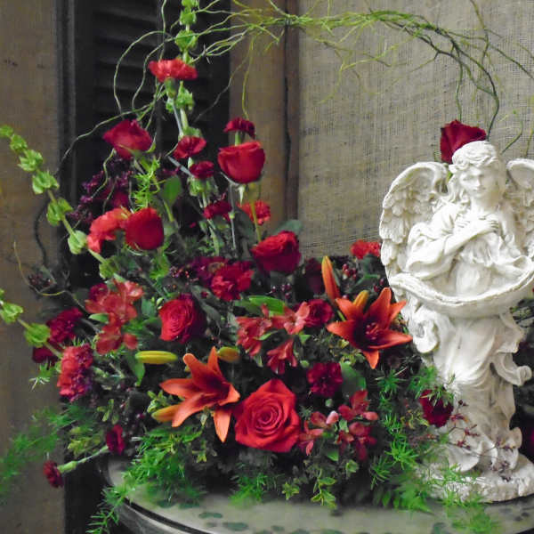 Red and orange floral arrangement beside a white angel statue