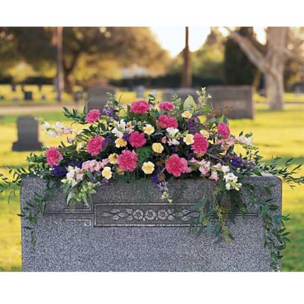 Cemetery saddle arrangement with pink, yellow, and white flowers on a gray headstone