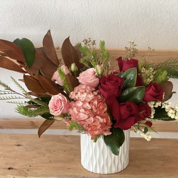Pink and red roses in a white textured vase with mixed greenery