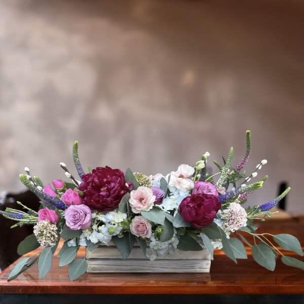 Low floral arrangement in a white wooden box with pink, purple, and white blooms