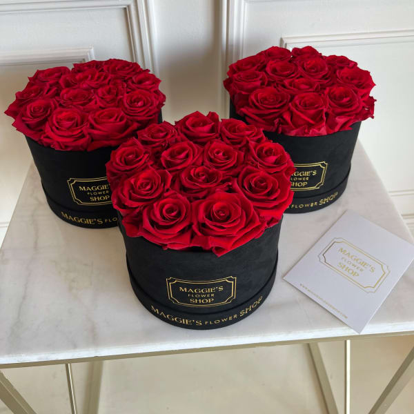 Three round boxes filled with red roses on a table