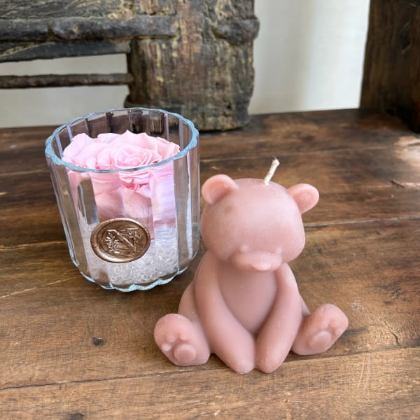 Pink rose in a glass votive beside a pink bear-shaped candle