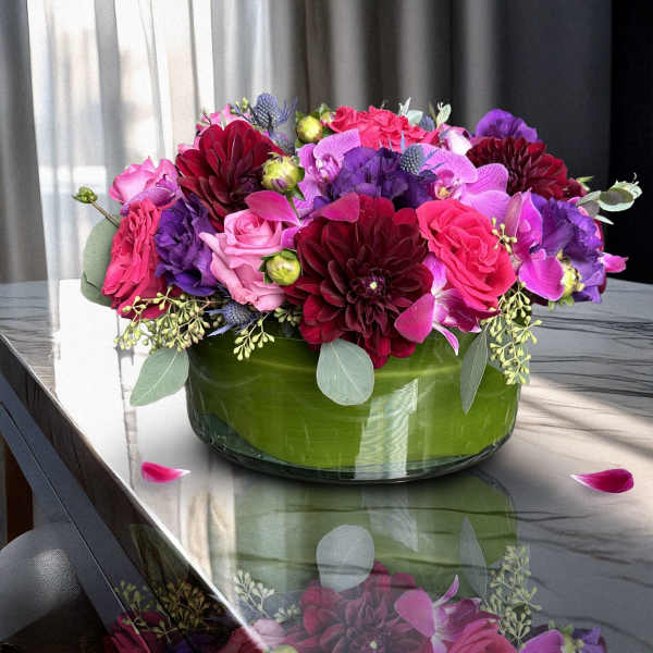 Pink, purple, and burgundy flowers arranged in a green glass bowl