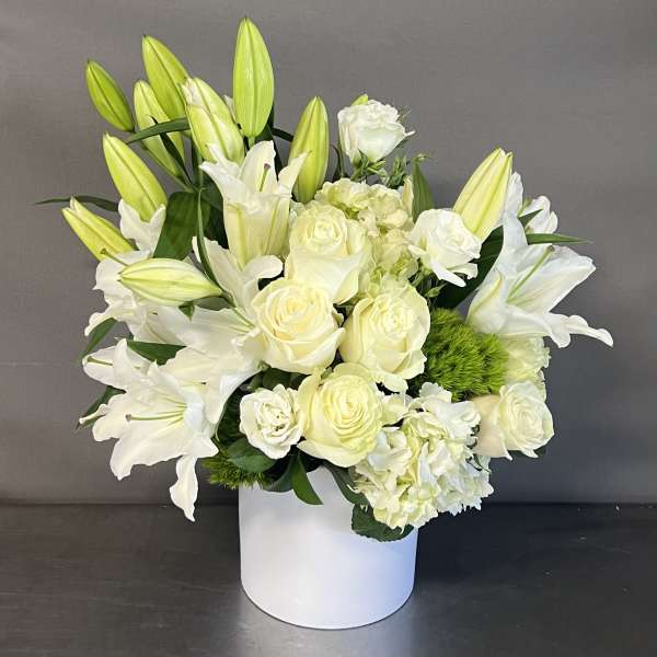 White lilies and roses arranged in a white vase.