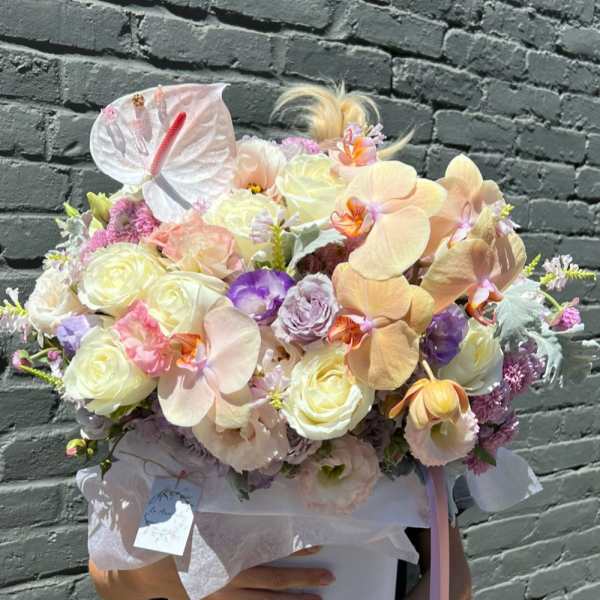 Pastel bouquet with orchids, roses, and a white anthurium in a round box