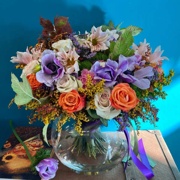 Mixed bouquet of purple, peach, and white flowers in a glass vase