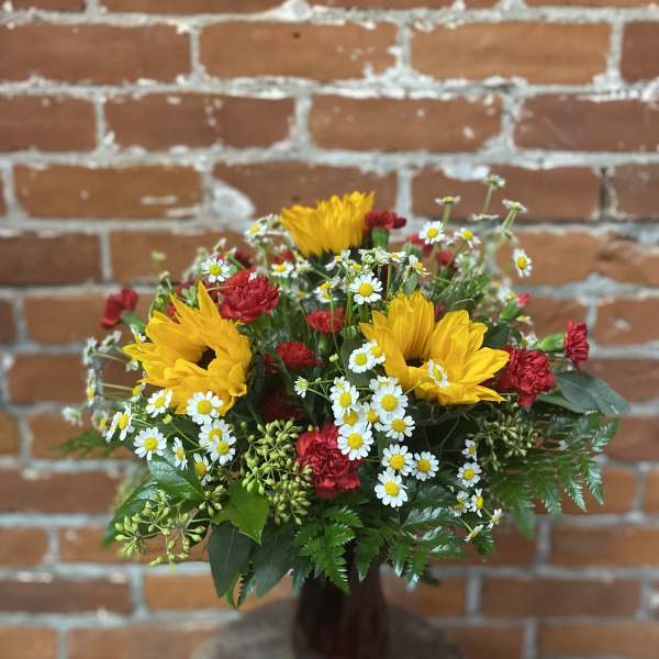 Bouquet of yellow sunflowers, red carnations, and white daisies in a brown vase