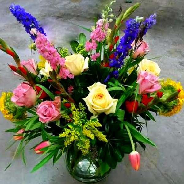 Mixed bouquet of roses and colorful tall blooms in a glass vase