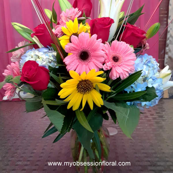 Mixed bouquet with roses, gerbera daisies, lilies, and hydrangeas in a glass vase