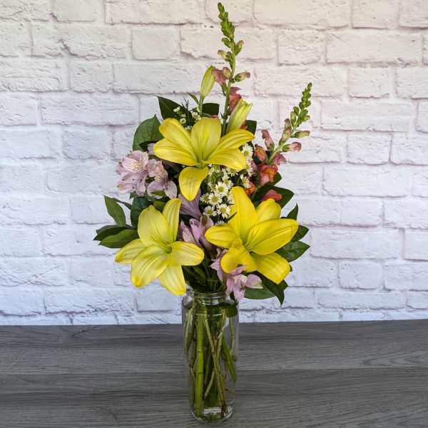 Yellow lilies and pink flowers arranged in a clear glass vase.