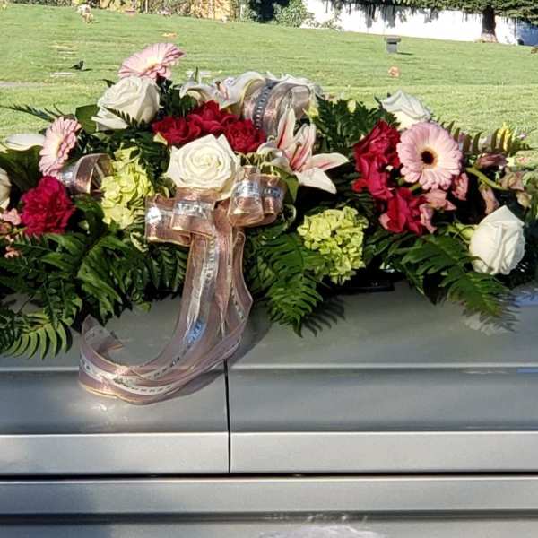 Casket spray with roses, lilies, gerbera daisies, and ribbon