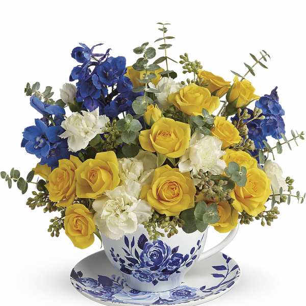 Yellow and blue roses with white carnations in a floral teacup and saucer