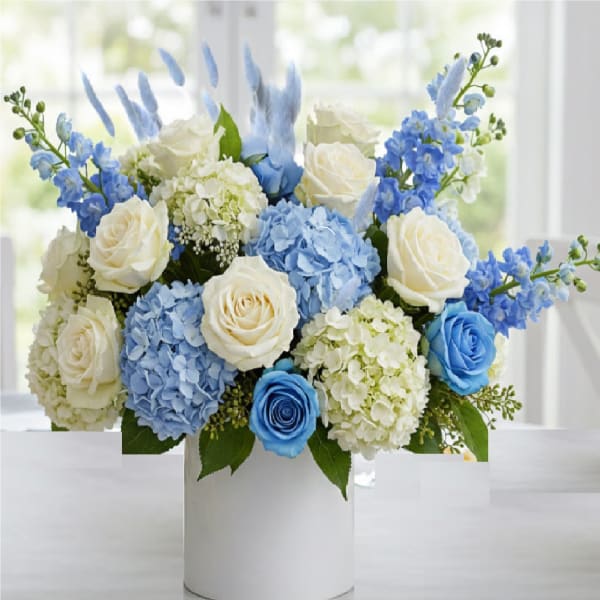 Round arrangement of white and blue roses with blue and ivory hydrangeas in a white cylinder vase