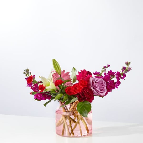 Mixed bouquet of pink, red, and white flowers in a pink glass vase