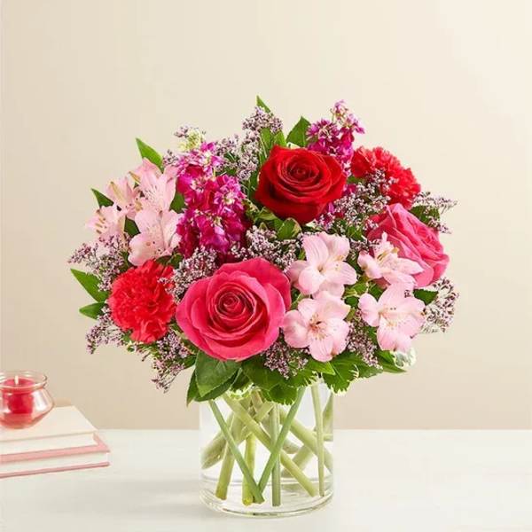 Bouquet of pink and red roses with small pink flowers in a clear glass vase