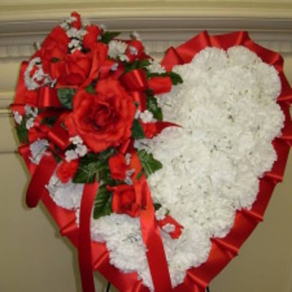 Heart-shaped floral tribute with red roses and white flowers on a stand