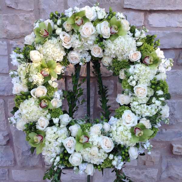 White floral wreath on a stand with roses and orchids