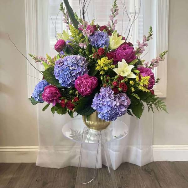 Large floral arrangement in a gold vase with blue, pink, and white blooms