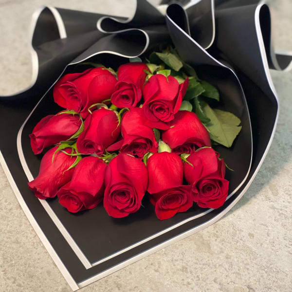 Dozen red roses wrapped in black paper with white trim on a stone surface