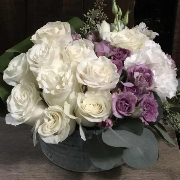 White and lavender roses arranged in a low round box