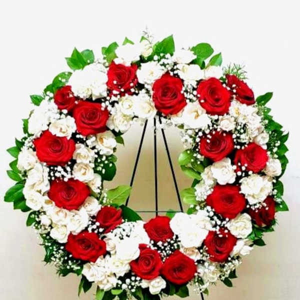 Standing wreath of red and white roses with white filler flowers on a metal easel.