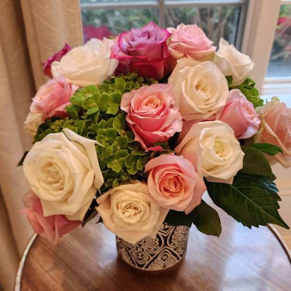 Compact arrangement of pink and white roses with green blooms in a patterned ceramic vase
