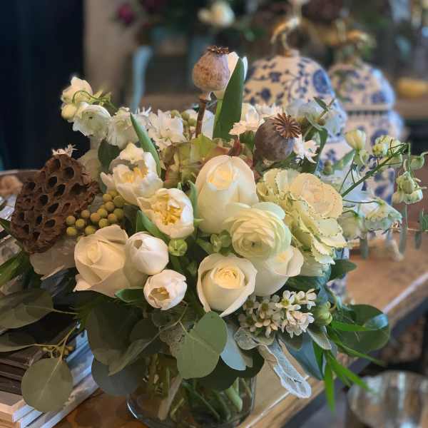 White floral arrangement in a glass vase with seed pods and greenery