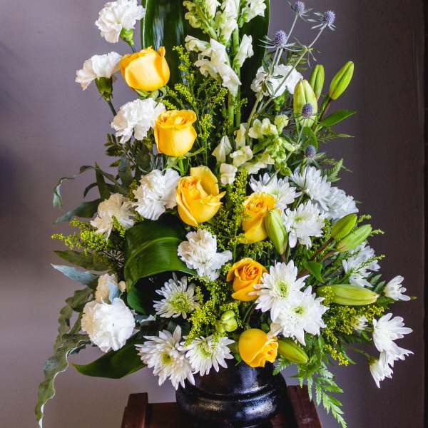 Tall floral arrangement with yellow roses, white blooms, and a black vase