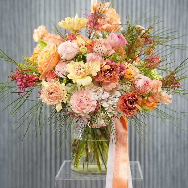Peach and pink bouquet in a glass vase with long ribbon tails