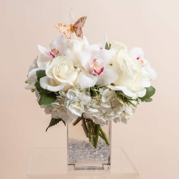 White floral arrangement in a clear square vase with a butterfly topper