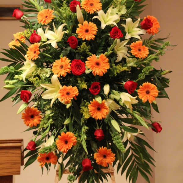 Large standing floral spray with red roses, orange gerberas, and white lilies