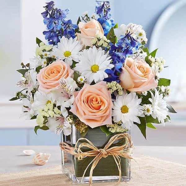 Peach roses and white daisies in a clear square vase with a bow